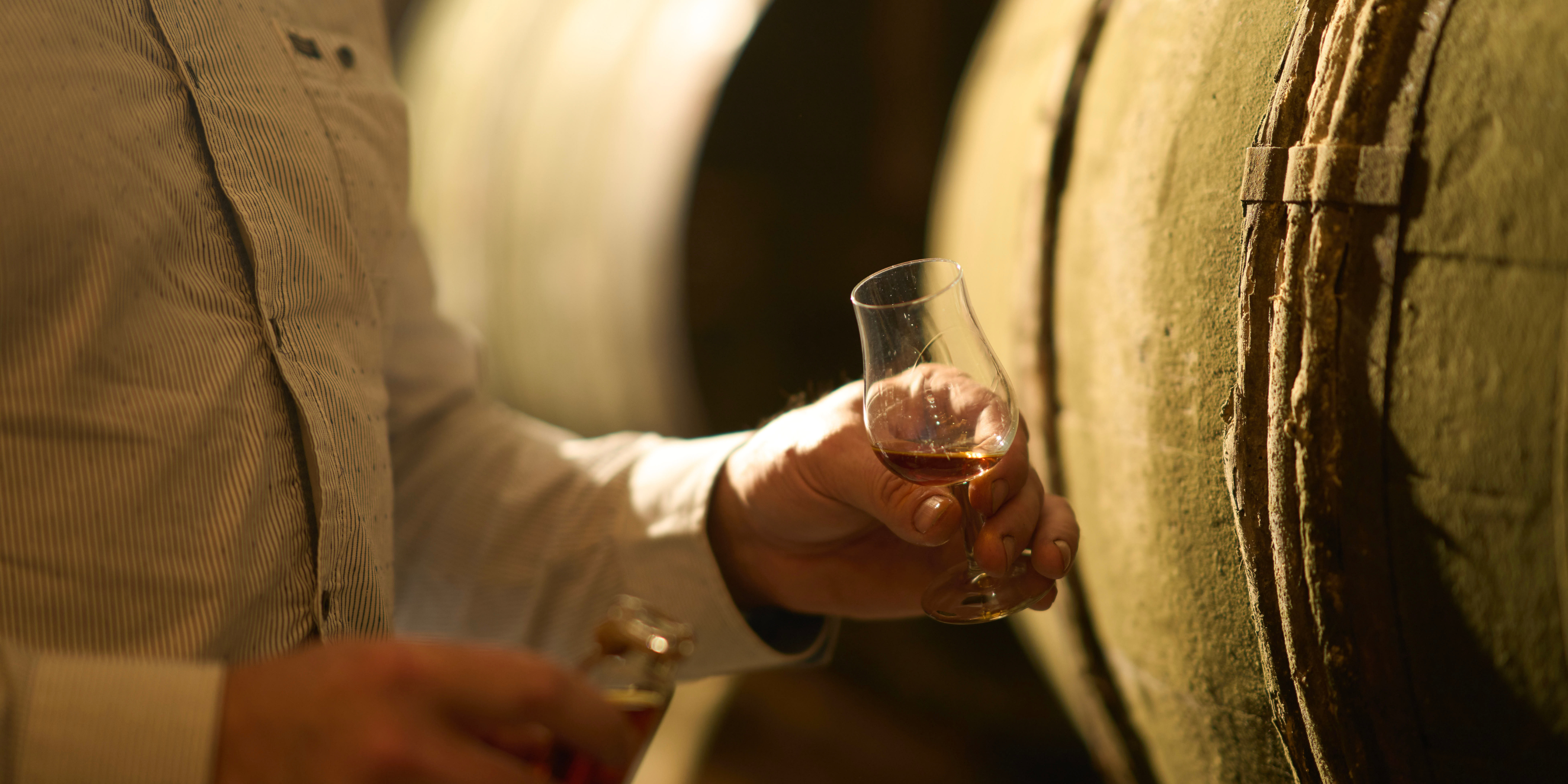 Close-up of a cellar master tasting aged cognac from a barrel at Maison Hardy.
