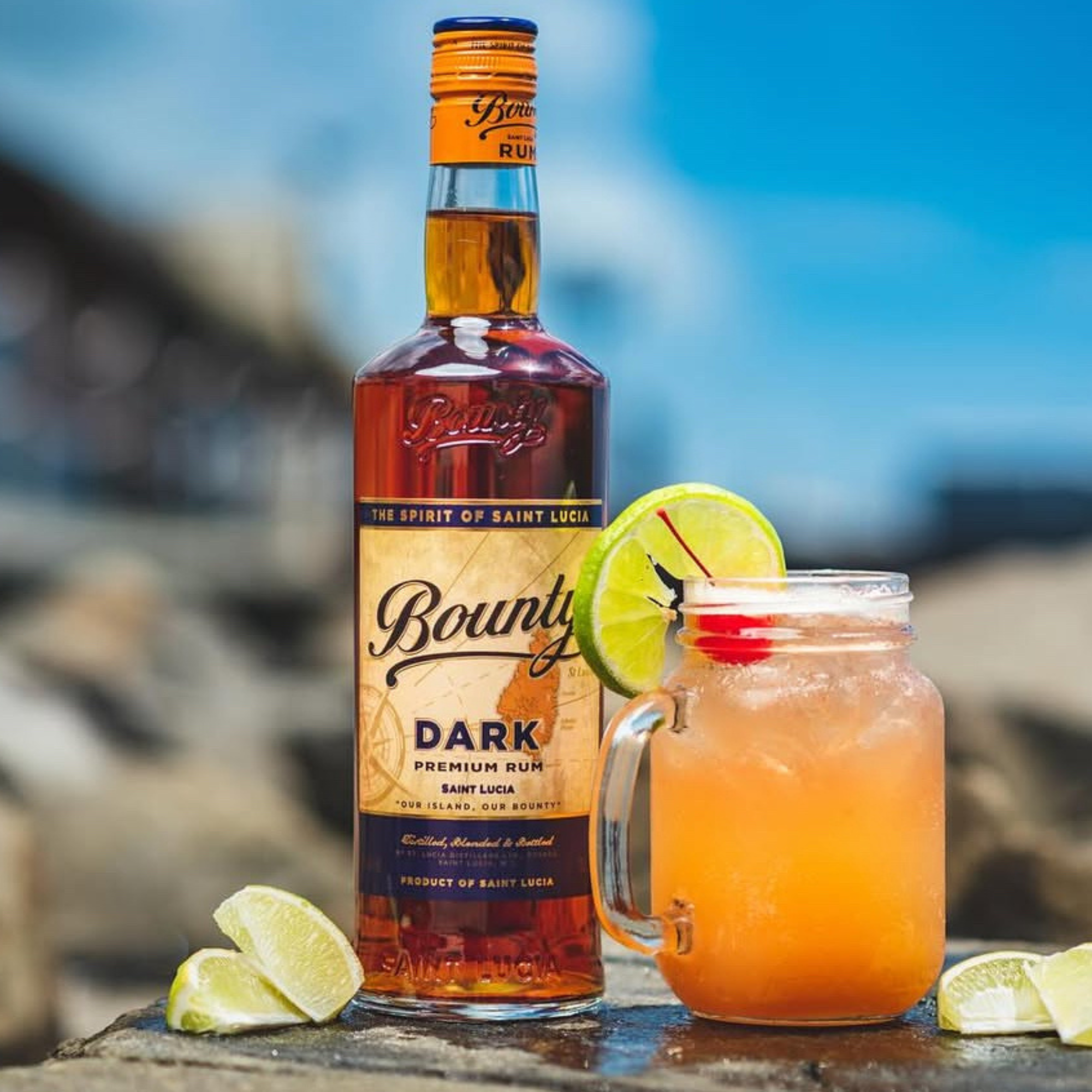 Bounty Dark Premium Rum bottle with a cocktail garnished with lime and red straw on a blurred natural background