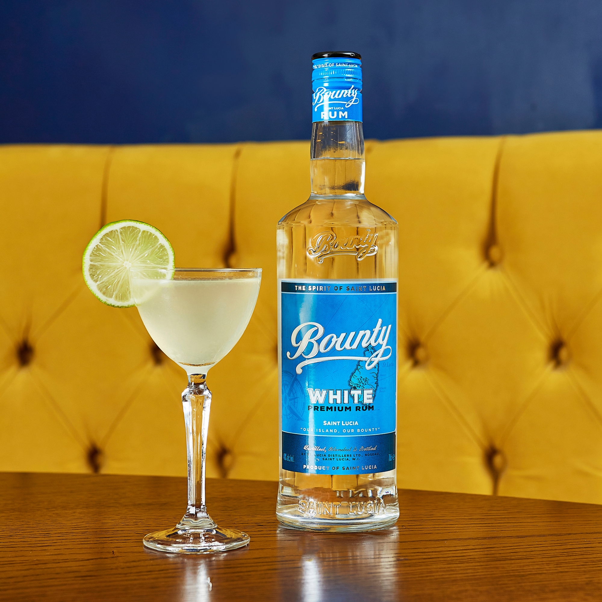 Bounty White Premium Rum bottle with a cocktail garnished with a lime wheel on a wooden surface.