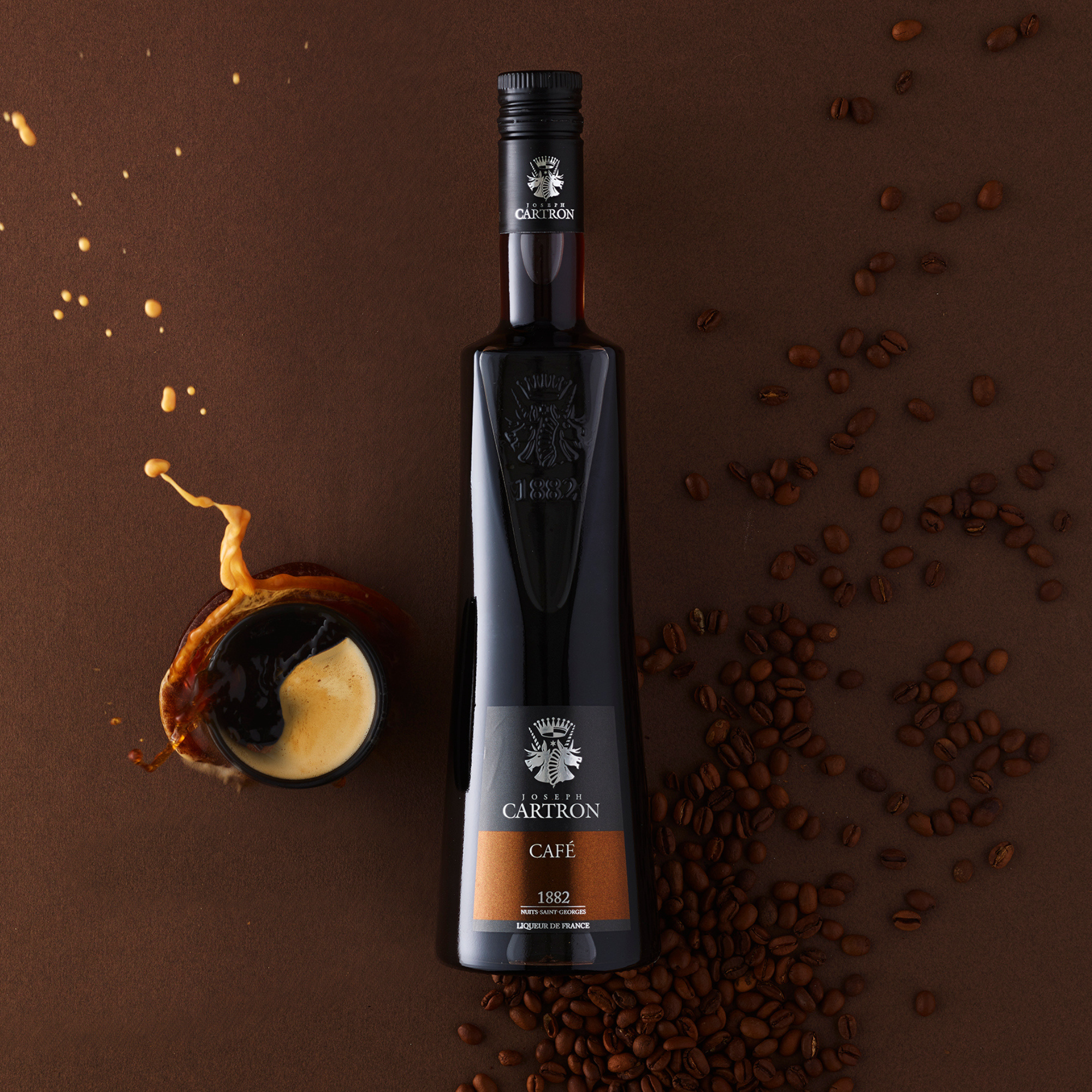 Bottle of Cartron coffee liqueur with coffee beans and a shot glass on a brown background