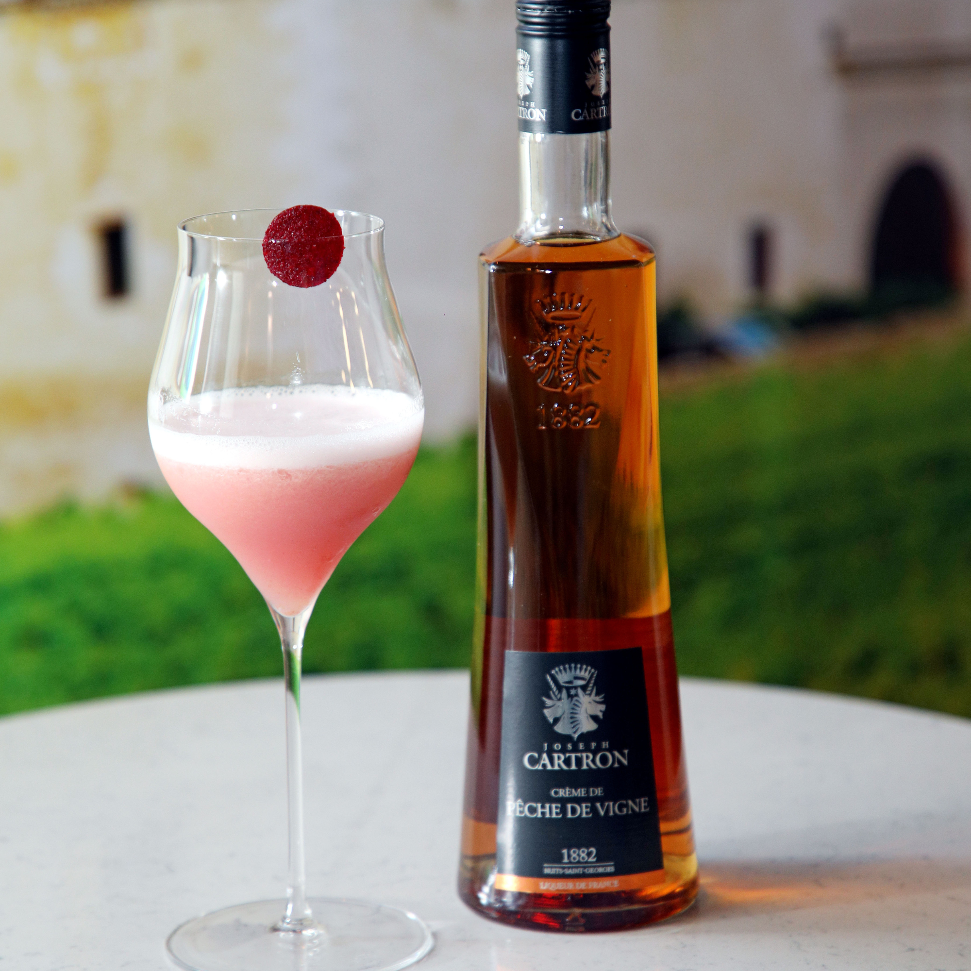 Bottle of Cartron liqueur with a pink cocktail on a blurred outdoor background