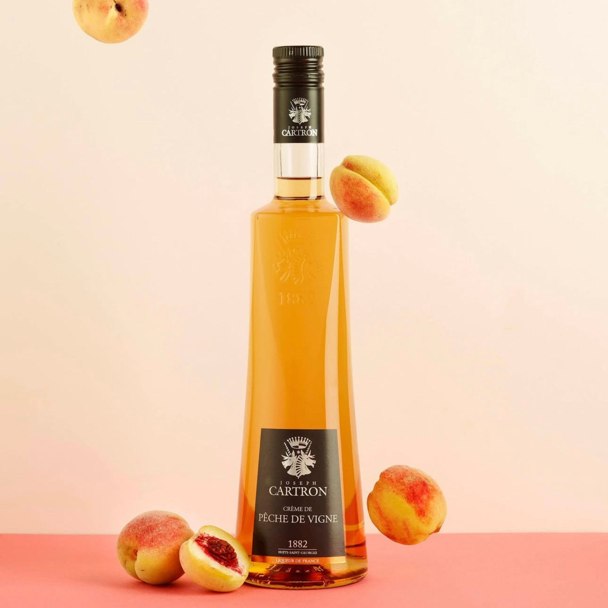 Bottle of Cartron wine with peaches on a pink background