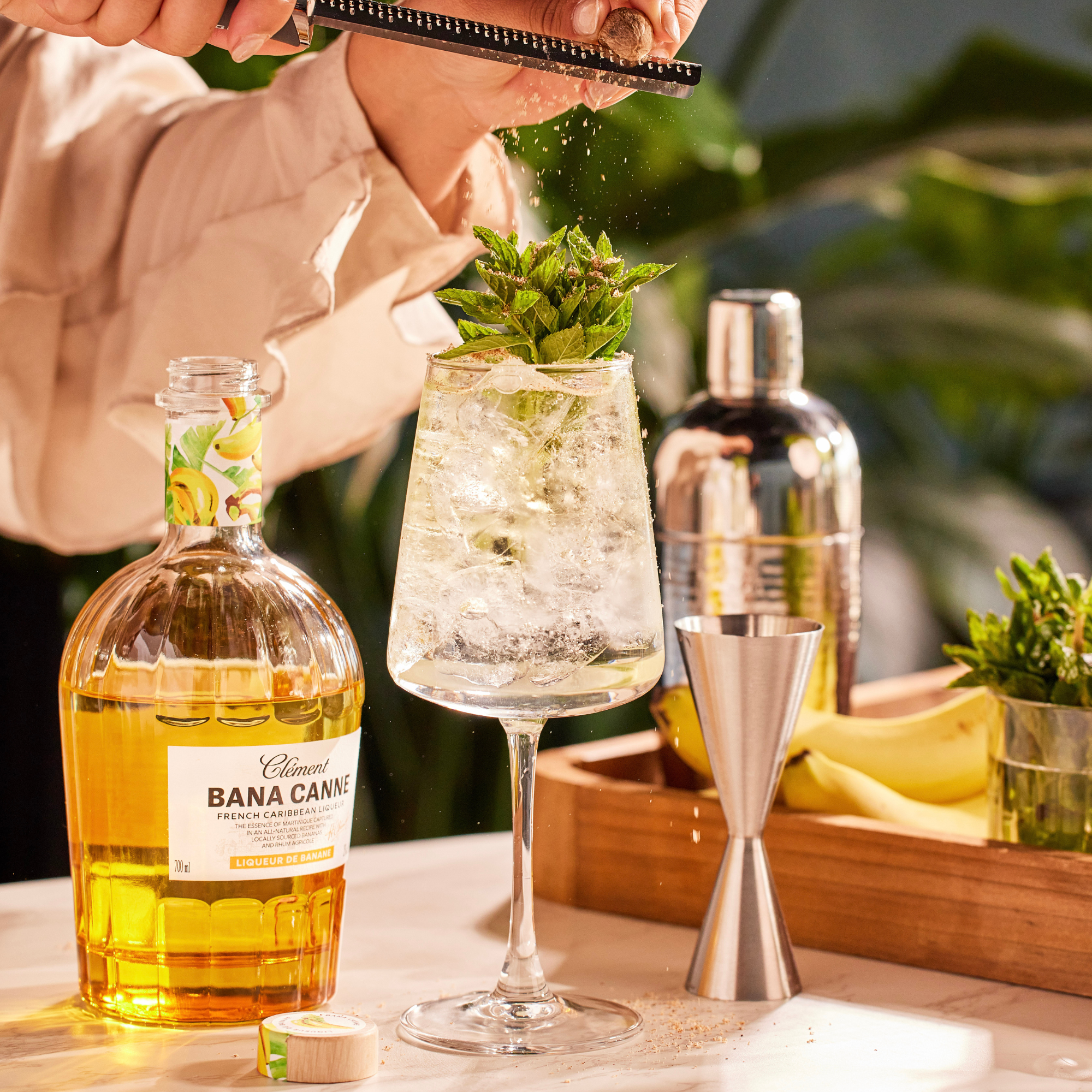 Person preparing a cocktail with Bana Cana rum bottle and other ingredients on a table.