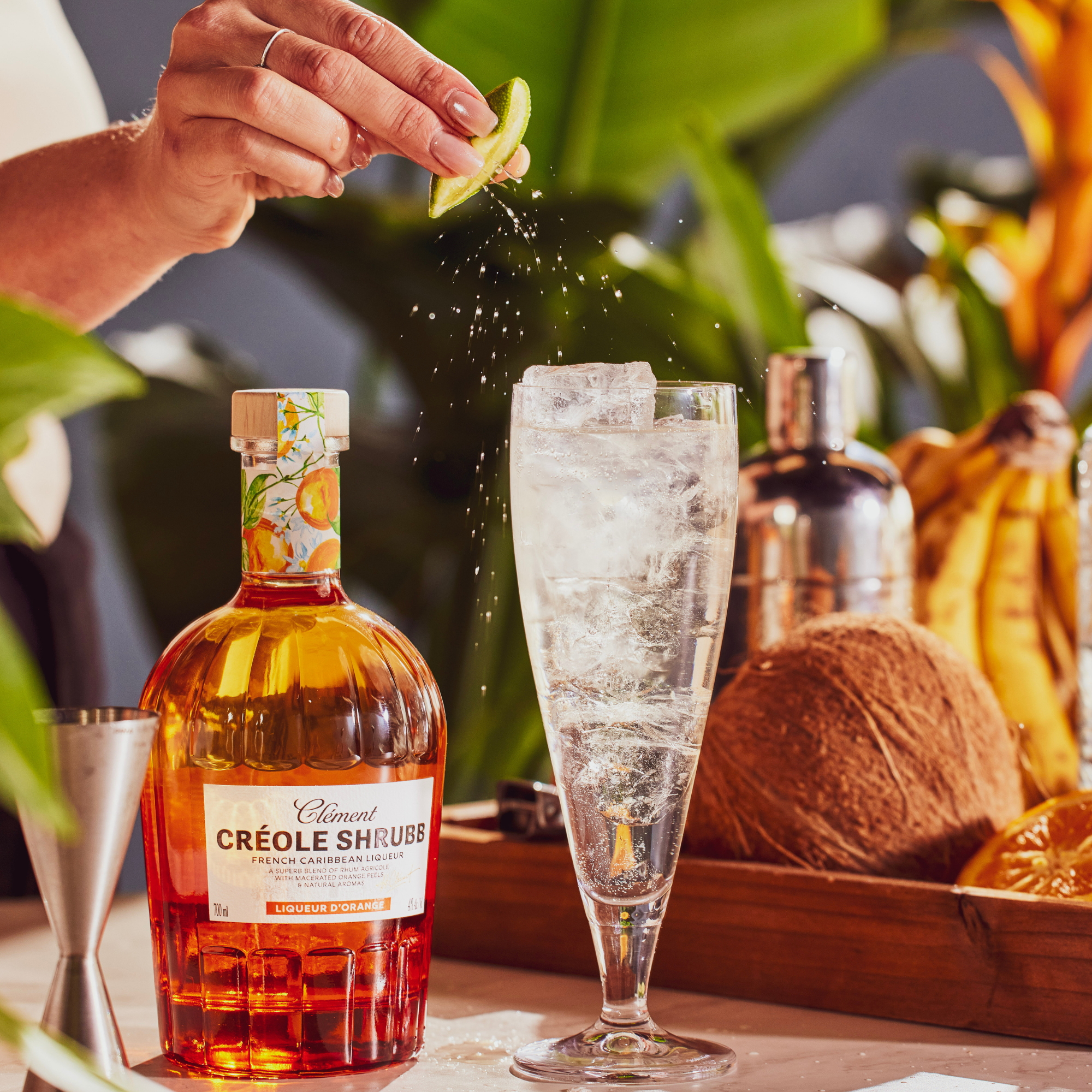 Person preparing a cocktail with Clément çrèole Shrubs bottle and a glass of sparkling drink.