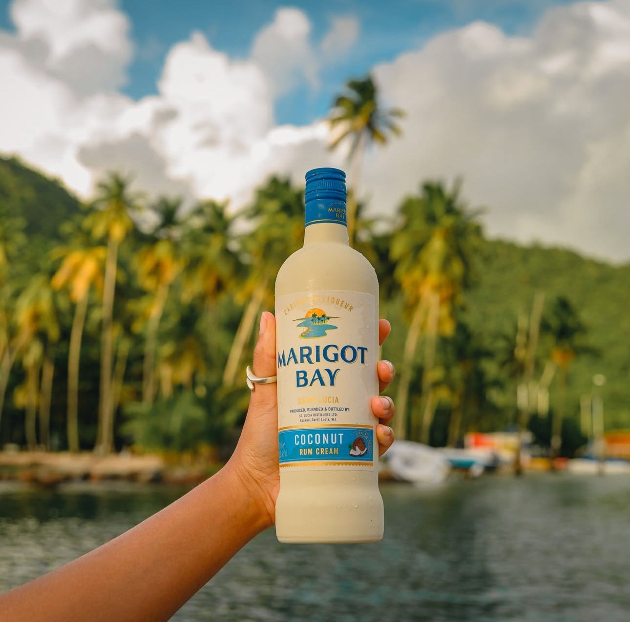 Person holding a bottle of Marigot Bay coconut rum cream with a tropical background