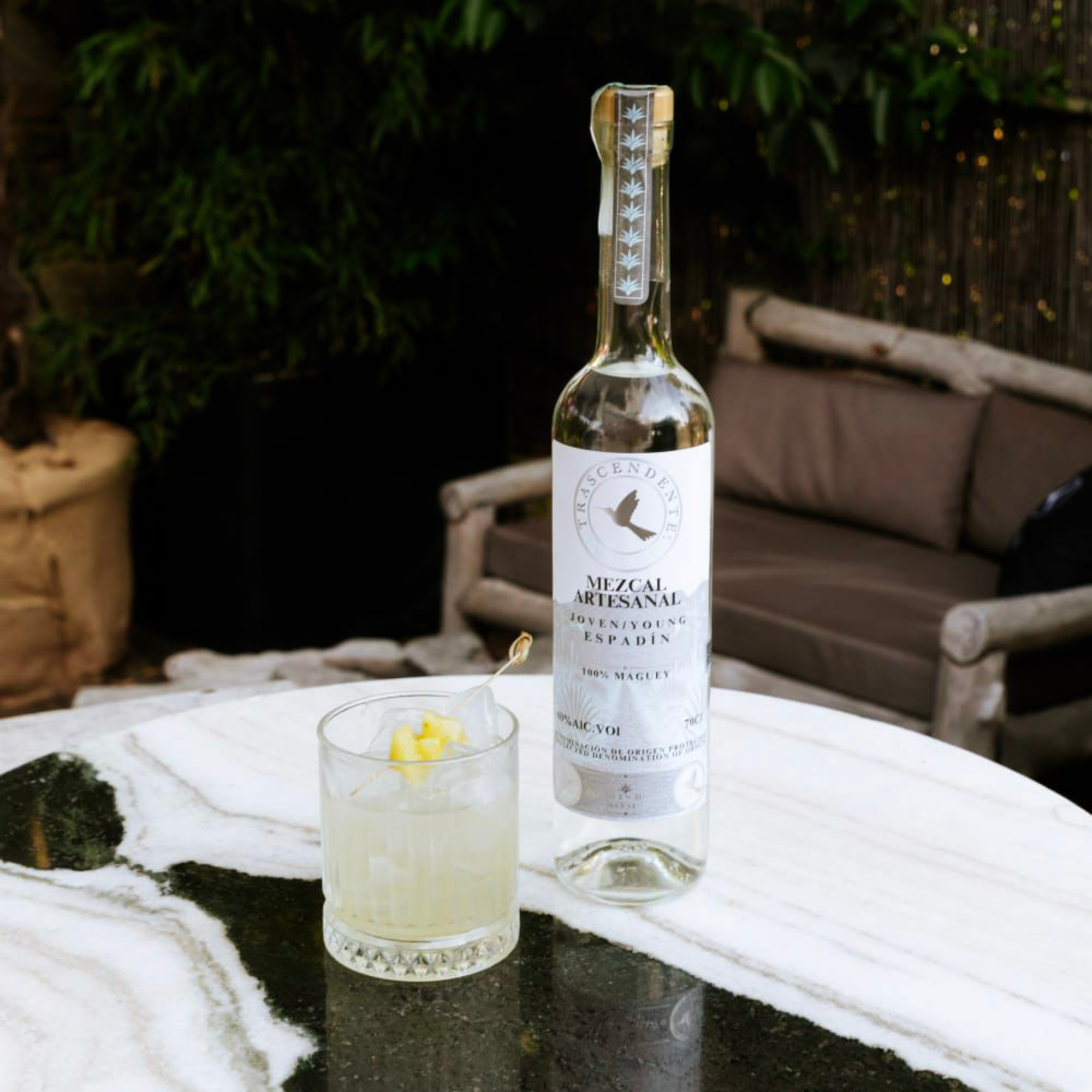 Bottle of Mezcal Artisanal Espadin on a table with a cocktail in an outdoor setting