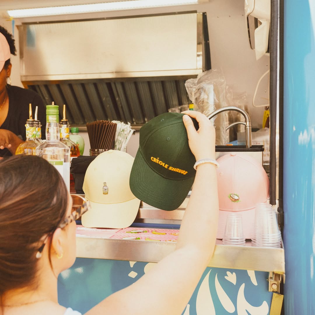 Person holding a green cap with 'CREOLE SHRUBB' branding.
