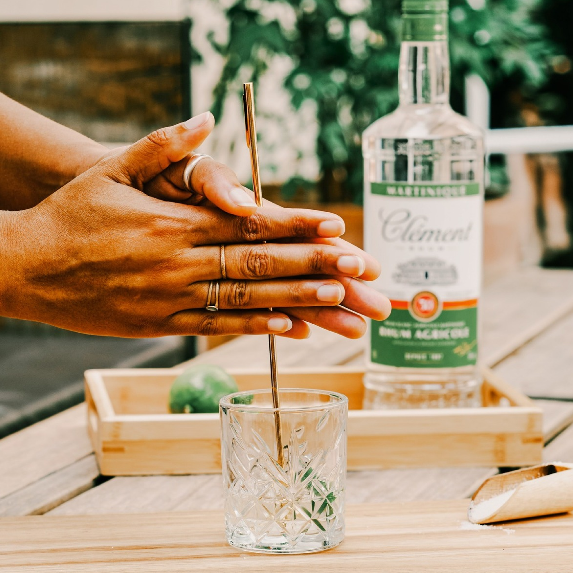 Person preparing a ti punch cocktail with a bottle of Clement blanc in the background.