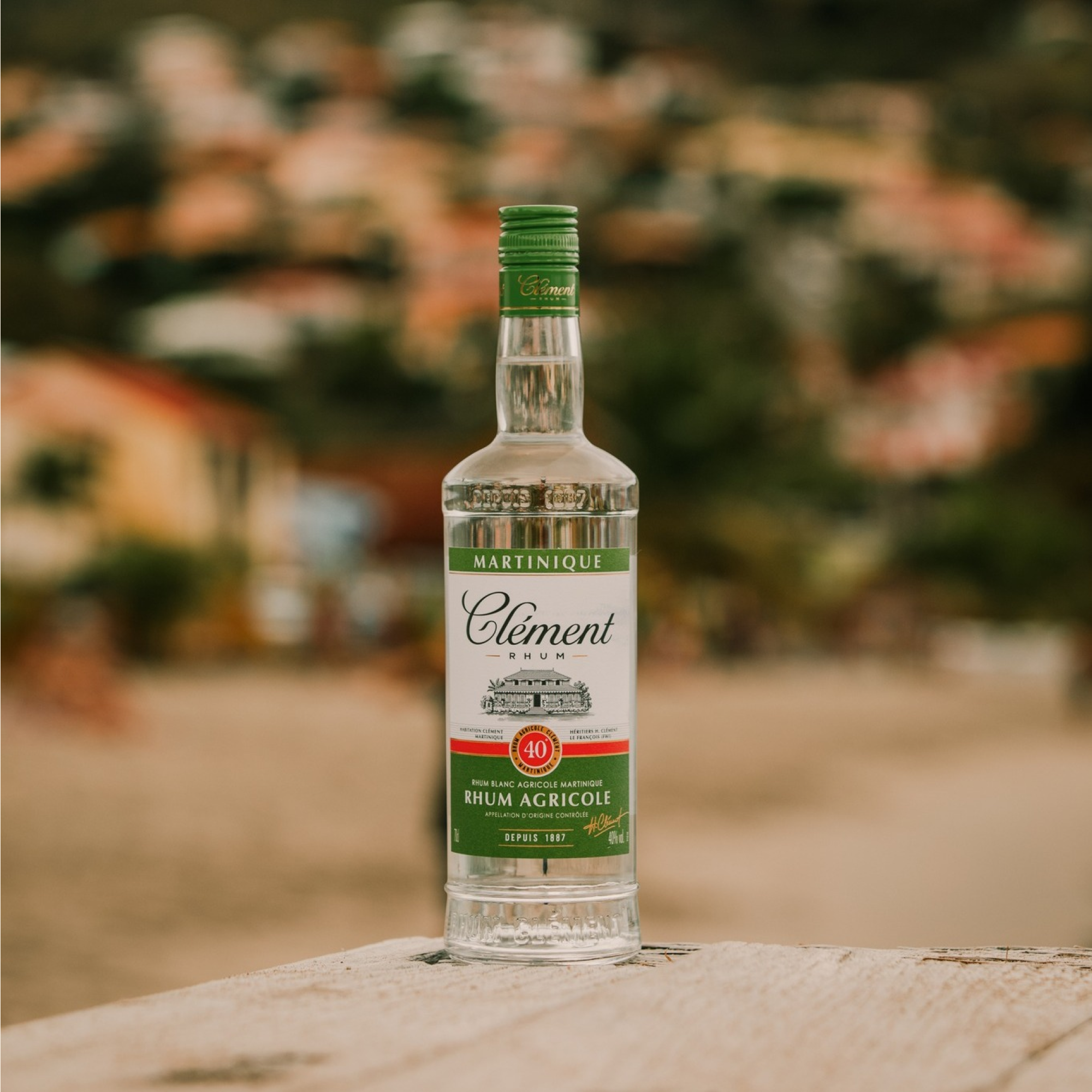 Bottle of Clément rhum agricole on a wooden surface with a blurred natural background