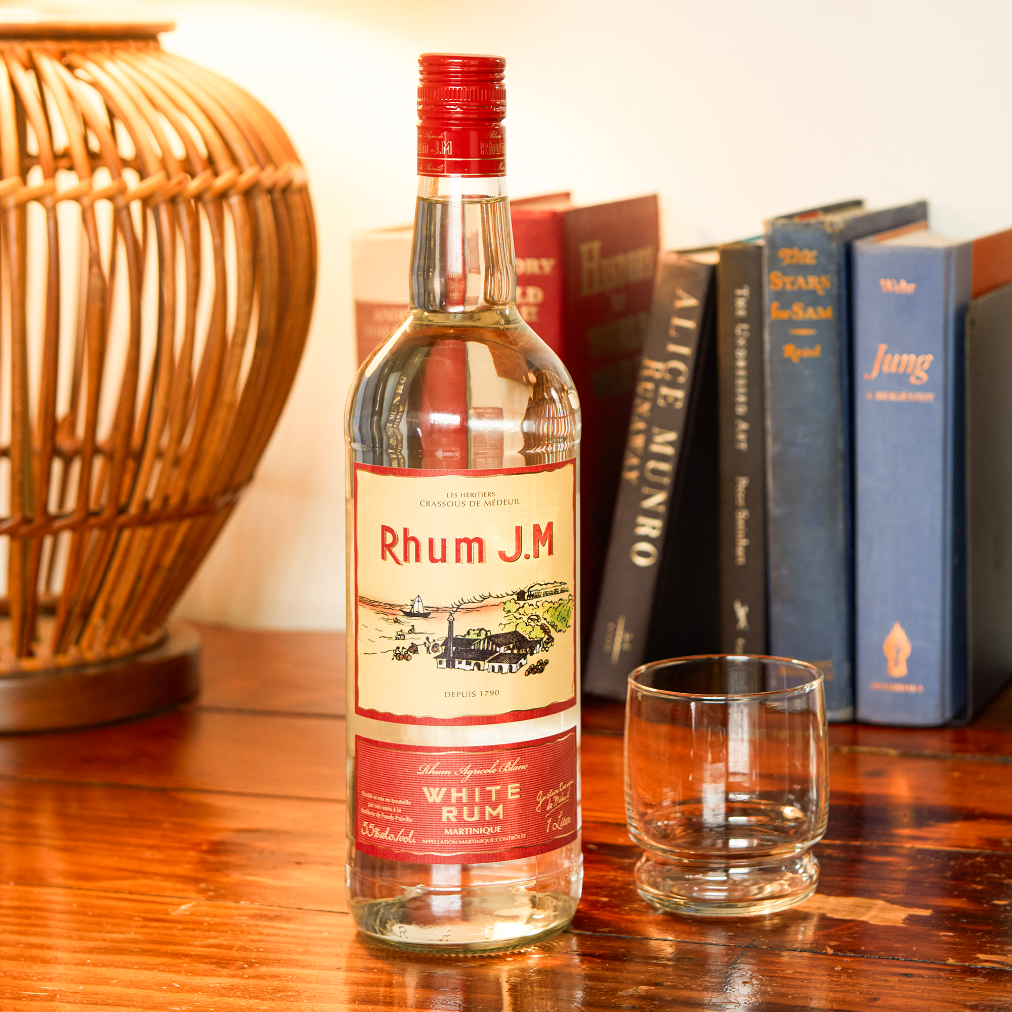 Rhum J.M. bottle with a glass on a wooden surface with books in the background