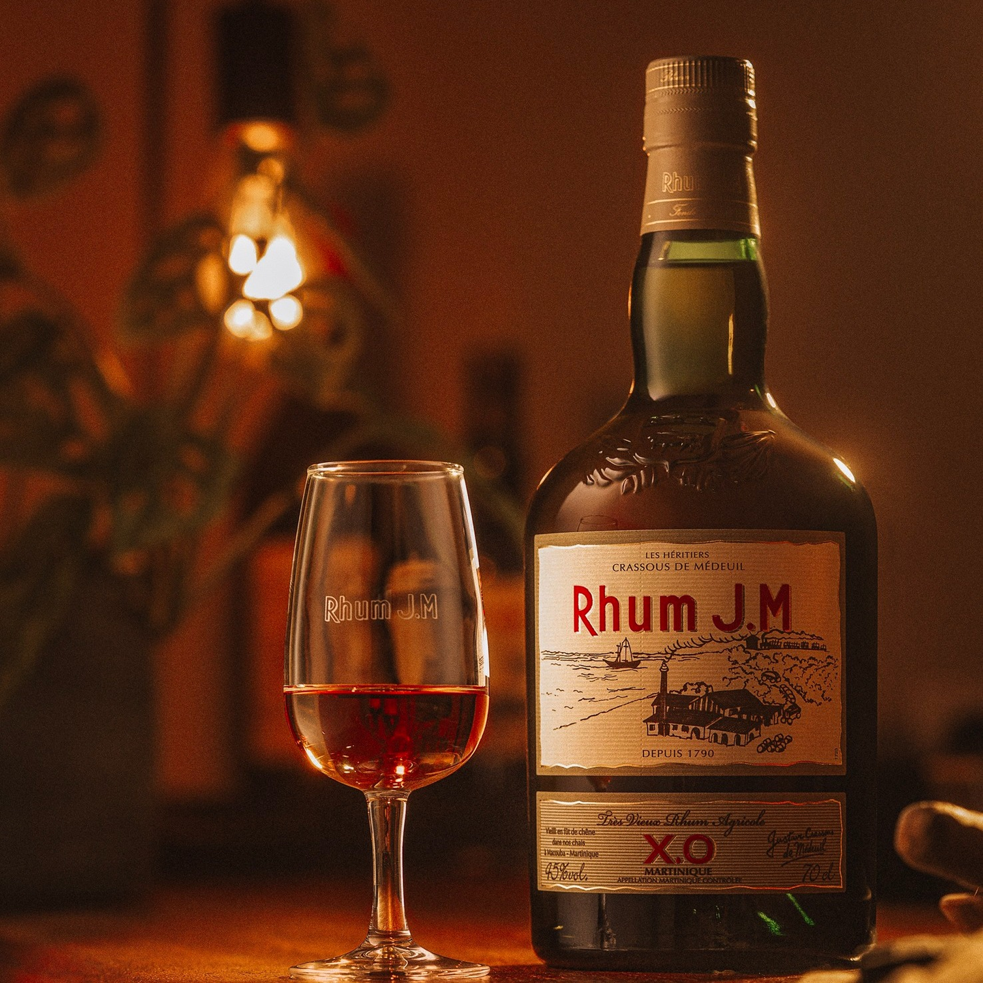Rhum J.M XO bottle with a glass of rum on a wooden surface, warm lighting.