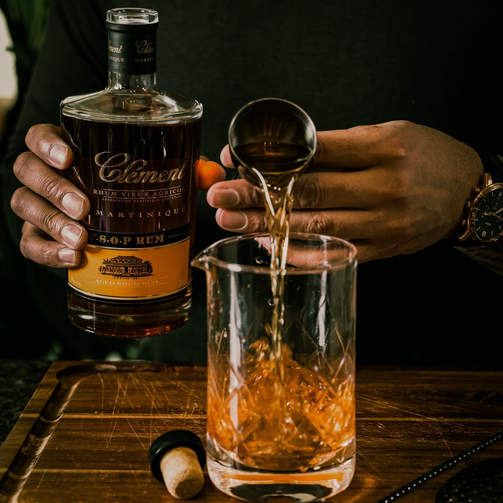 Person pouring rum from a bottle into a glass on a wooden surface.