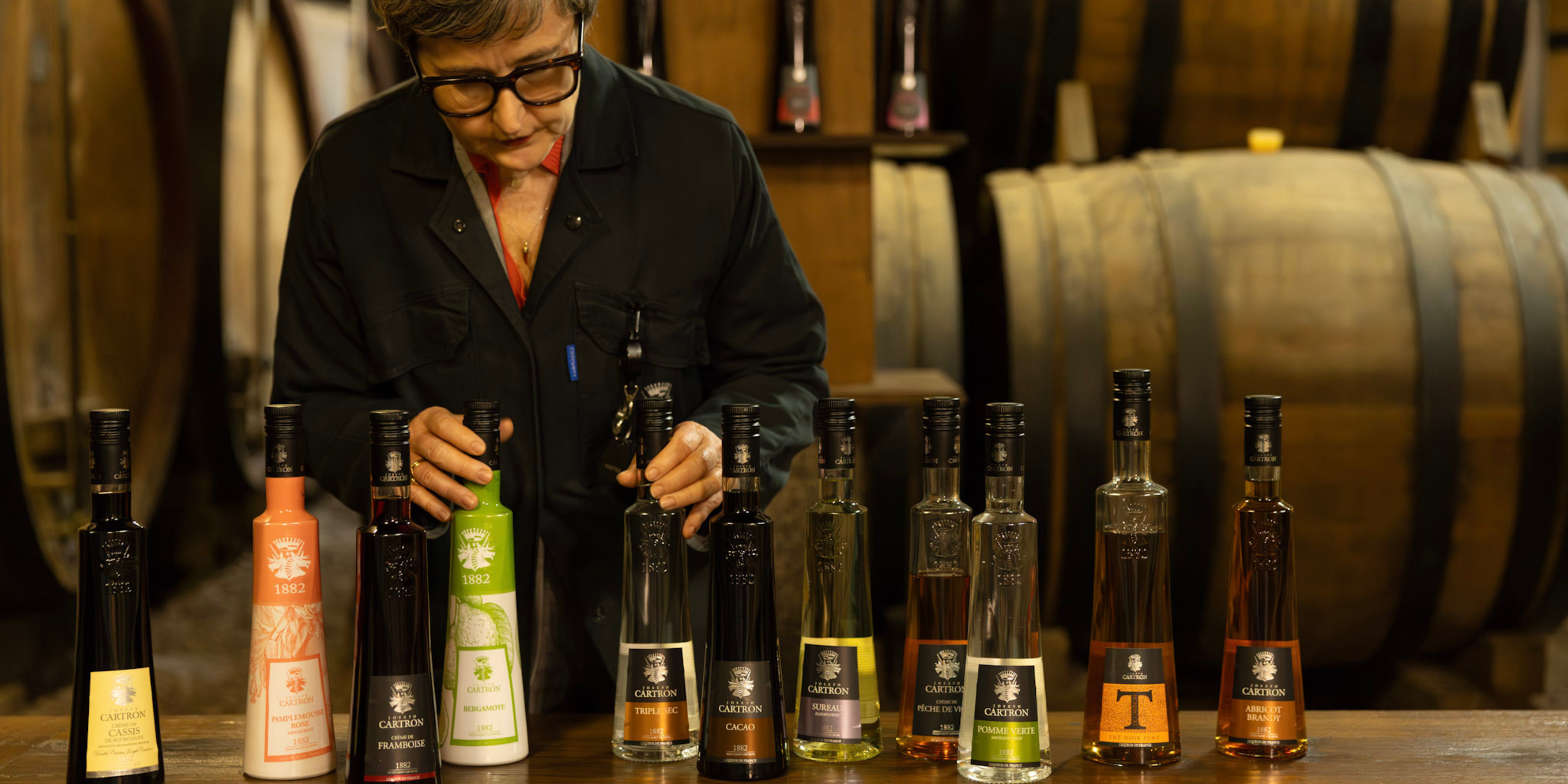 Master blender examining a selection of Joseph Cartron liqueurs and brandies in a Burgundy cellar surrounded by oak barrels
