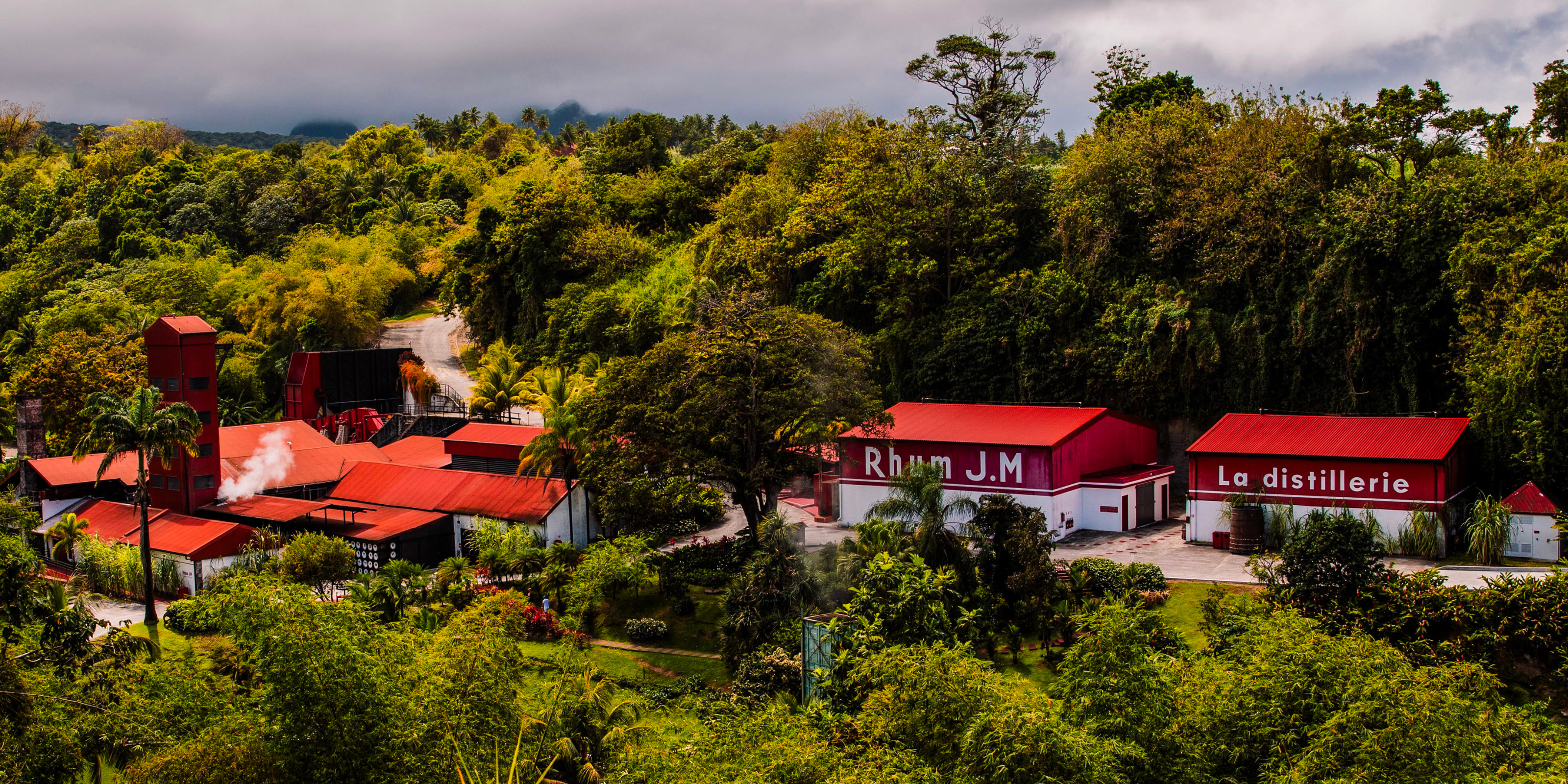 Aerial view of the Rhum J.M distillery in Martinique surrounded by lush tropical vegetation and red-roofed buildings.