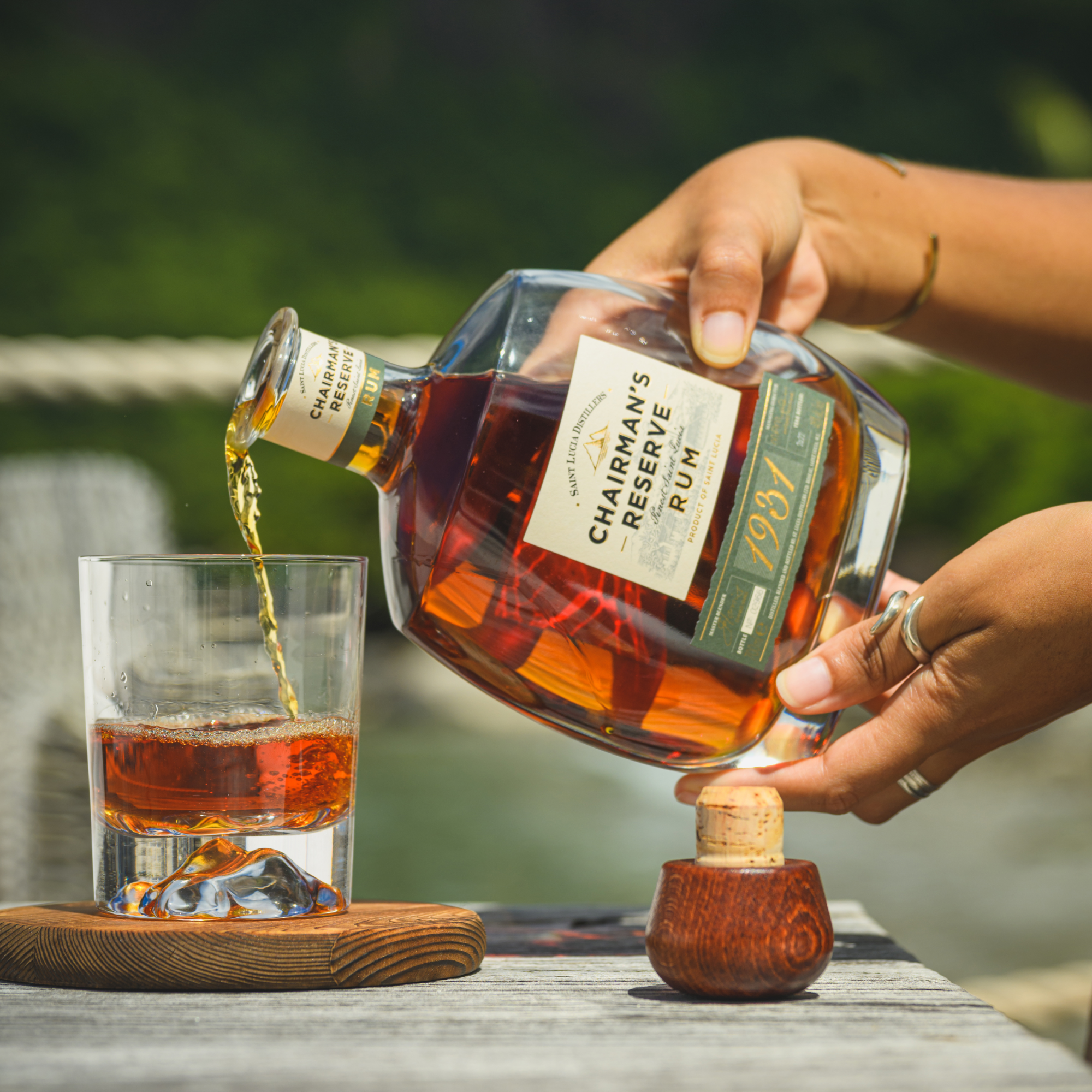 Person pouring Charman's Reserve 1931 Rum into a glass with a blurred outdoor background