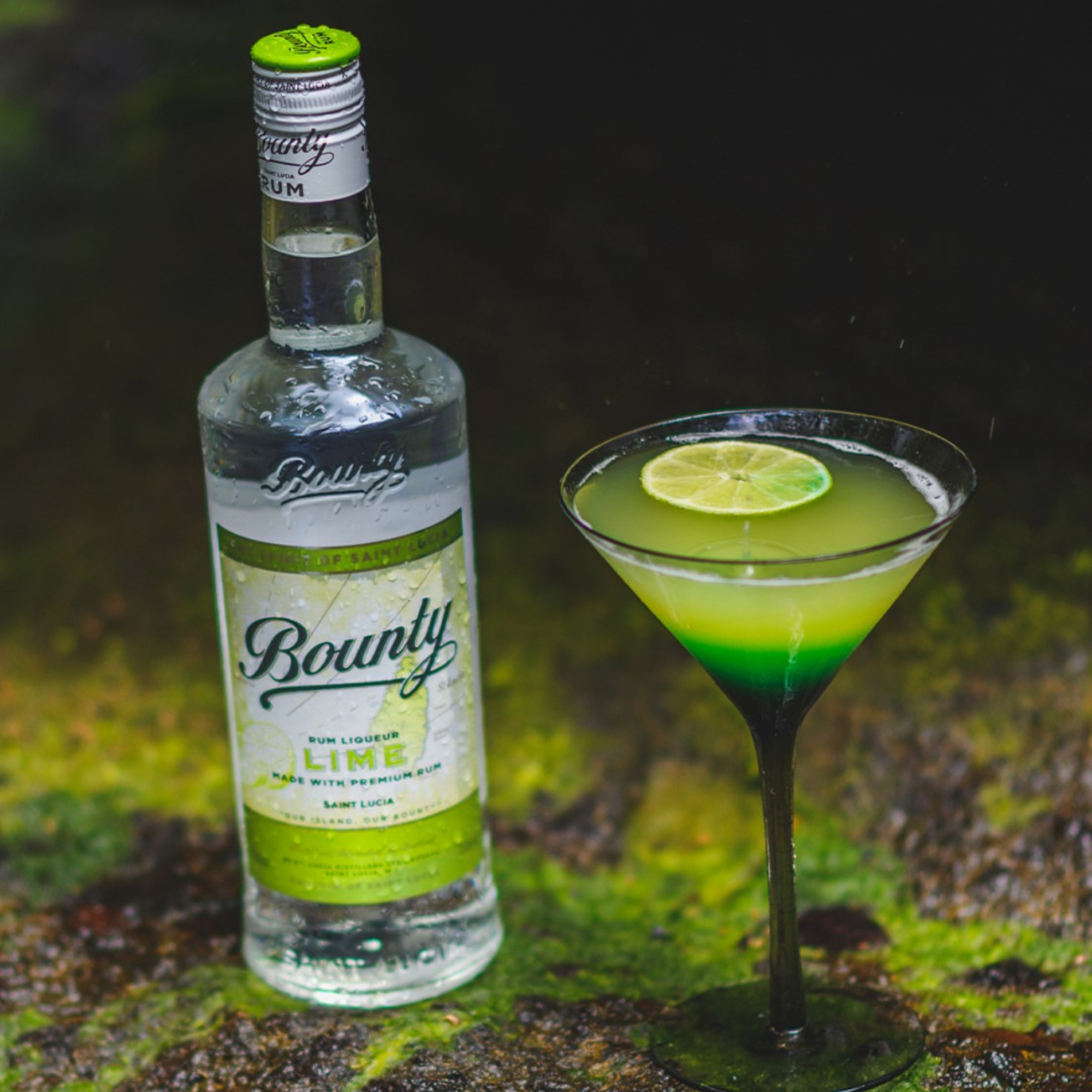 Bounty Lime bottle with a cocktail garnished with a lime wedge on a green background