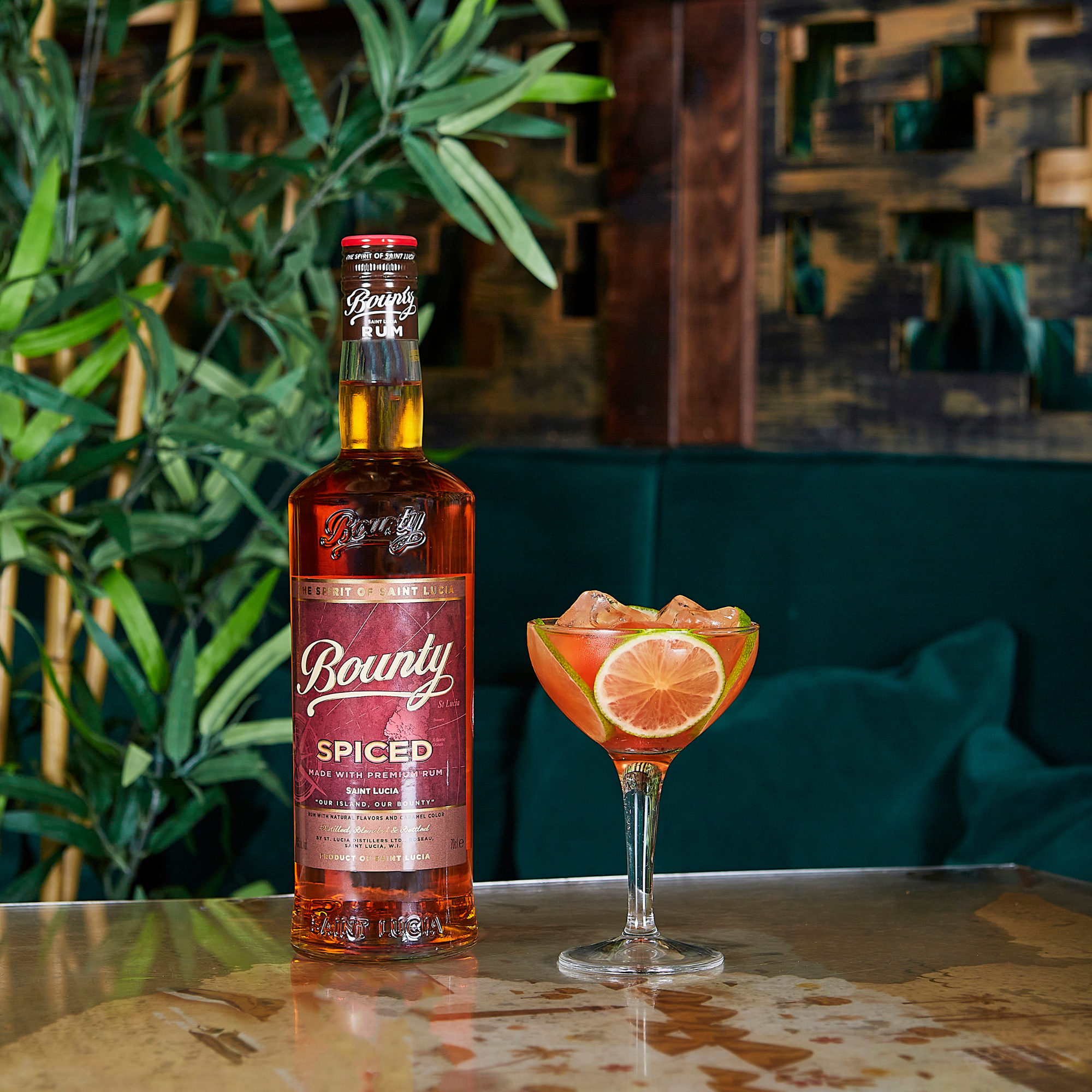 Bounty Spiced rum bottle with a cocktail on a table against a wooden wall and plant background
