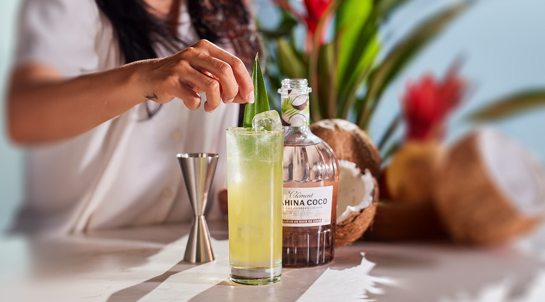 Person preparing a cocktail with a bottle of Mahina Coco in a tropical setting.