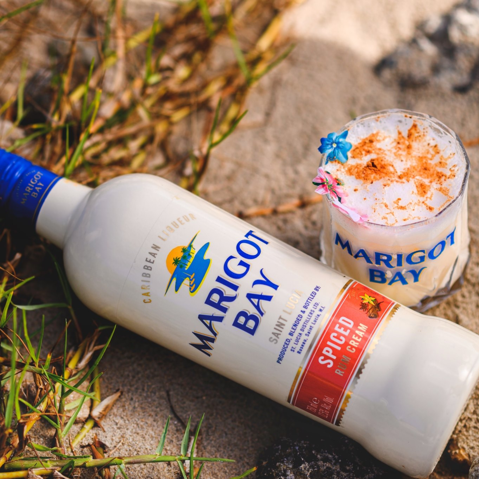 Marigot Bay spiced rum bottle and a cocktail on a sandy surface with grass.
