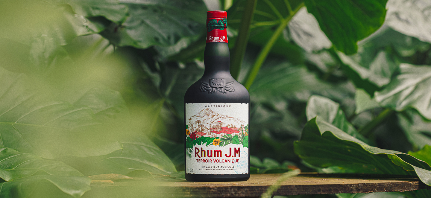 Rhum JM bottle on a wooden surface with green leaves in the background
