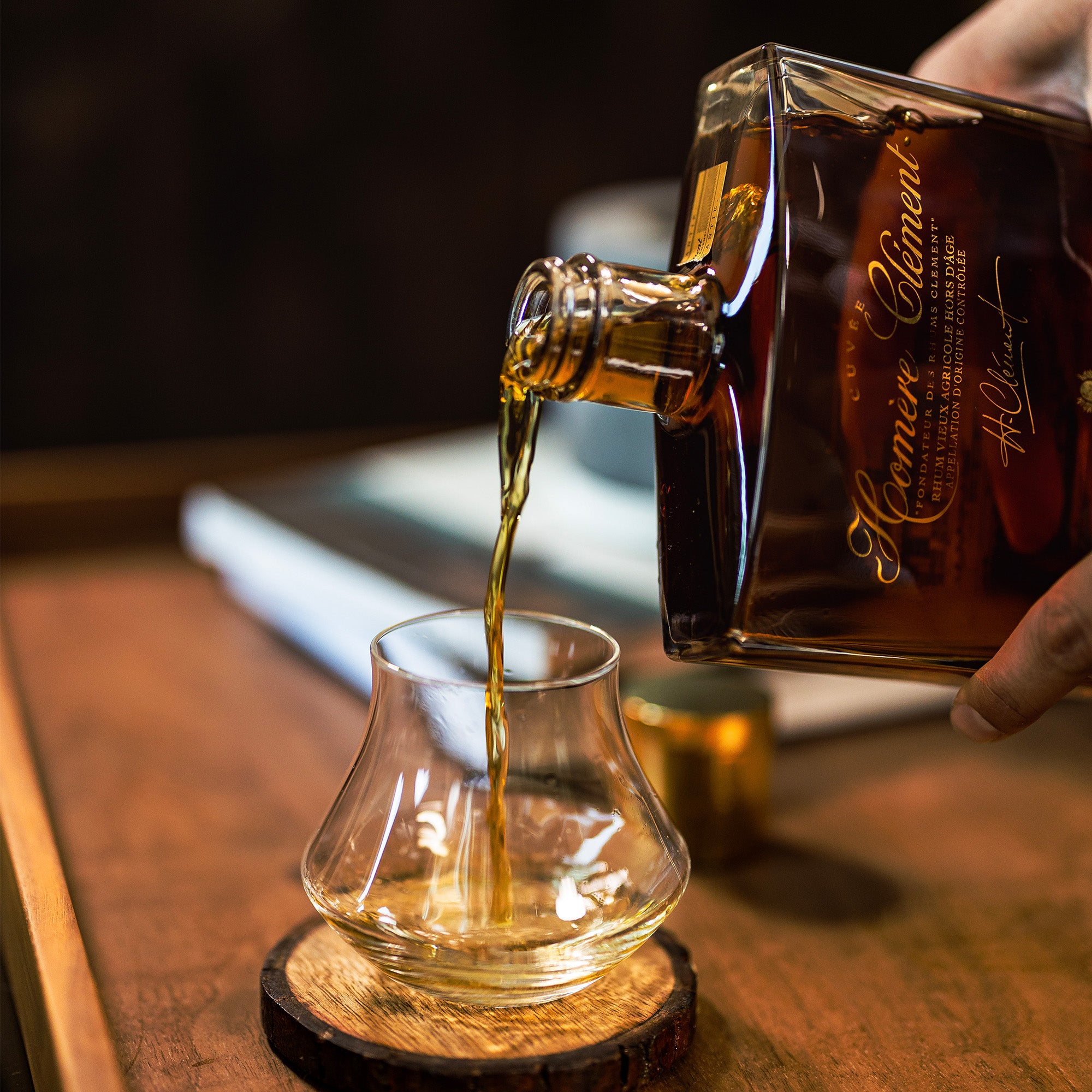 Whiskey being poured from a bottle into a glass on a wooden coaster.