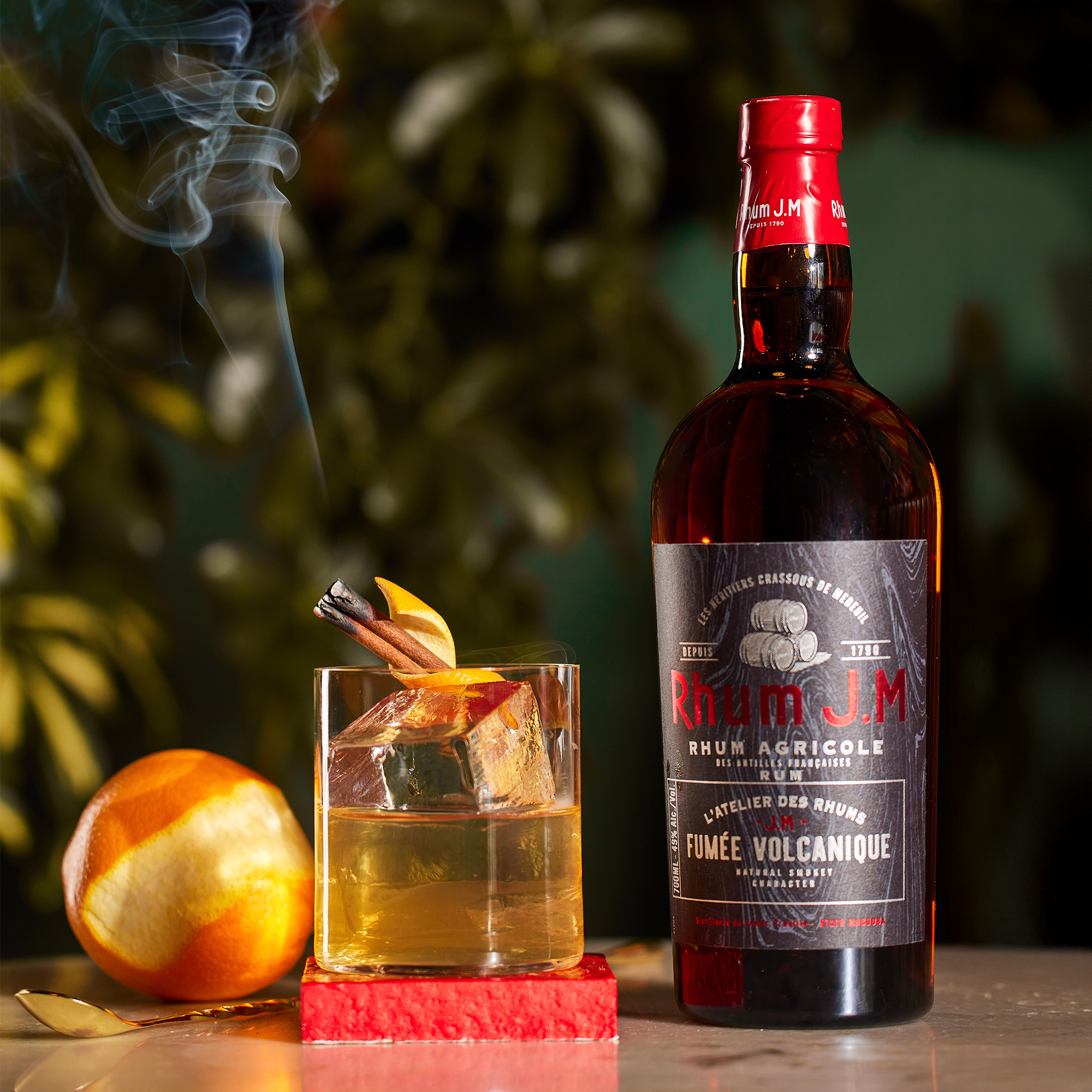 Bottle of Rum J.M. fumée with a cocktail and orange garnish on a dark background