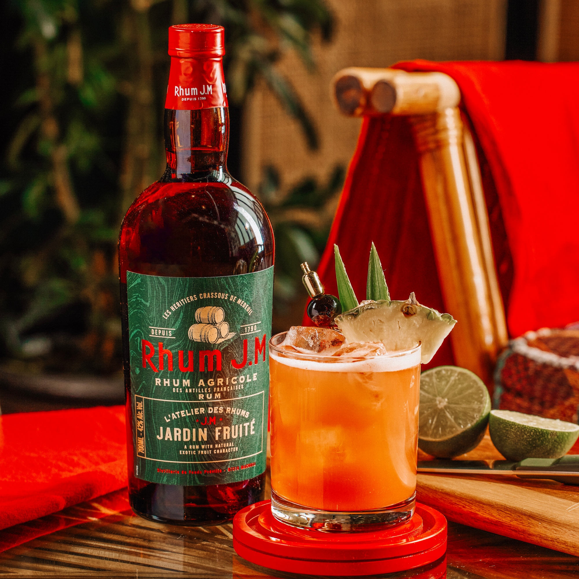 Bottle of Rhum J.M. with a cocktail garnished with fruit on a wooden table.