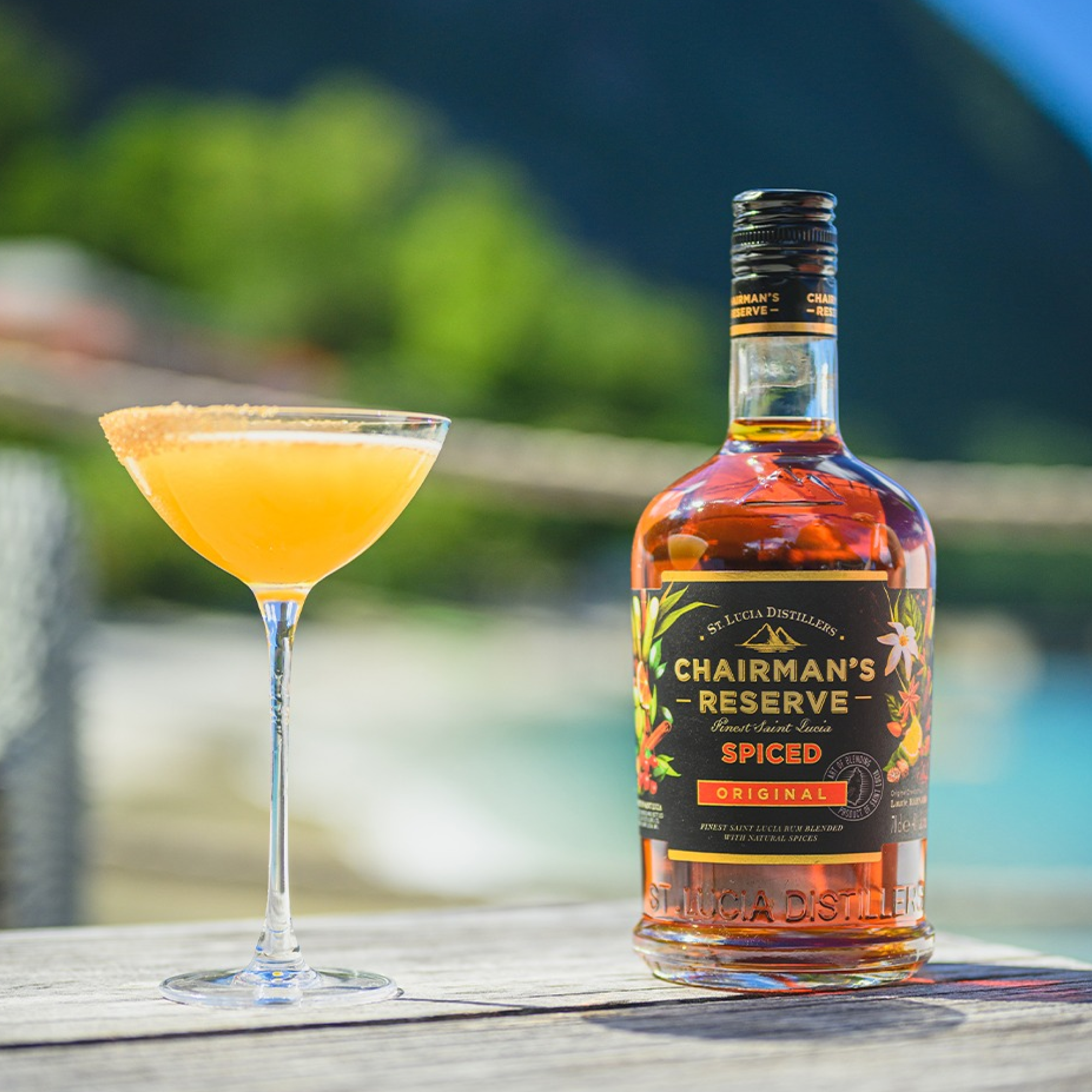 Bottle of Chairman's Reserve Spiced rum with a cocktail on a wooden surface outdoors.
