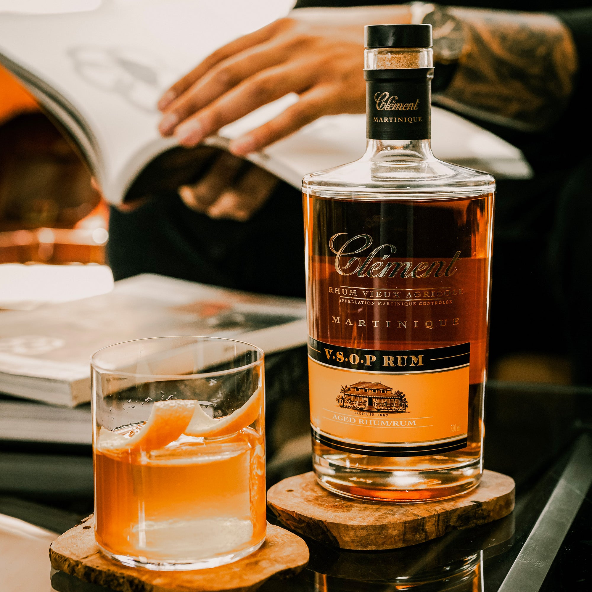 Clement VSOP rum bottle with a glass of rum on a wooden coaster, blurred background