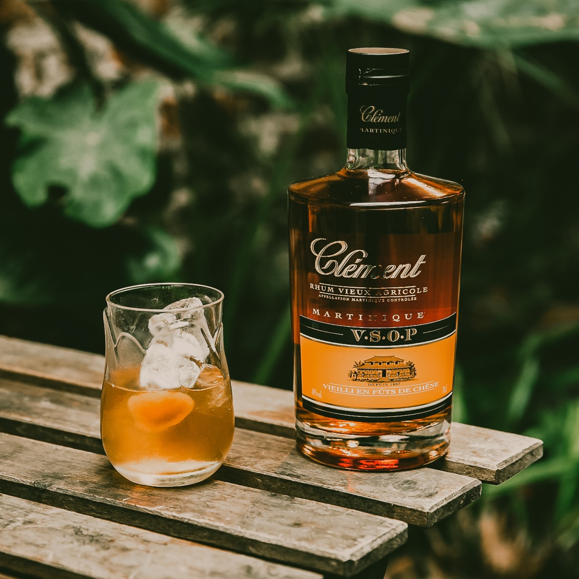 Bottle of Clément VSOP rum and a glass with a drink on a wooden surface.